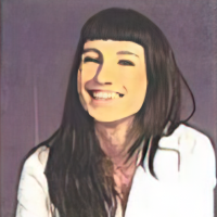 Person with long dark hair and bangs smiling, wearing a white shirt against a neutral background.