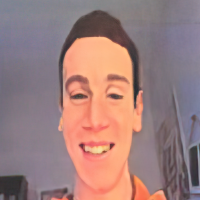 A person with short dark hair is smiling at the camera in an indoor setting.